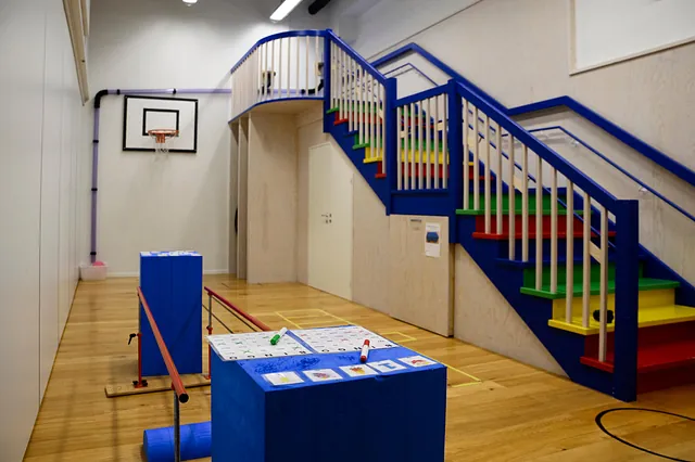 Gymsal med fargerik trapp, basketballkurv og balanseutstyr på tregulv